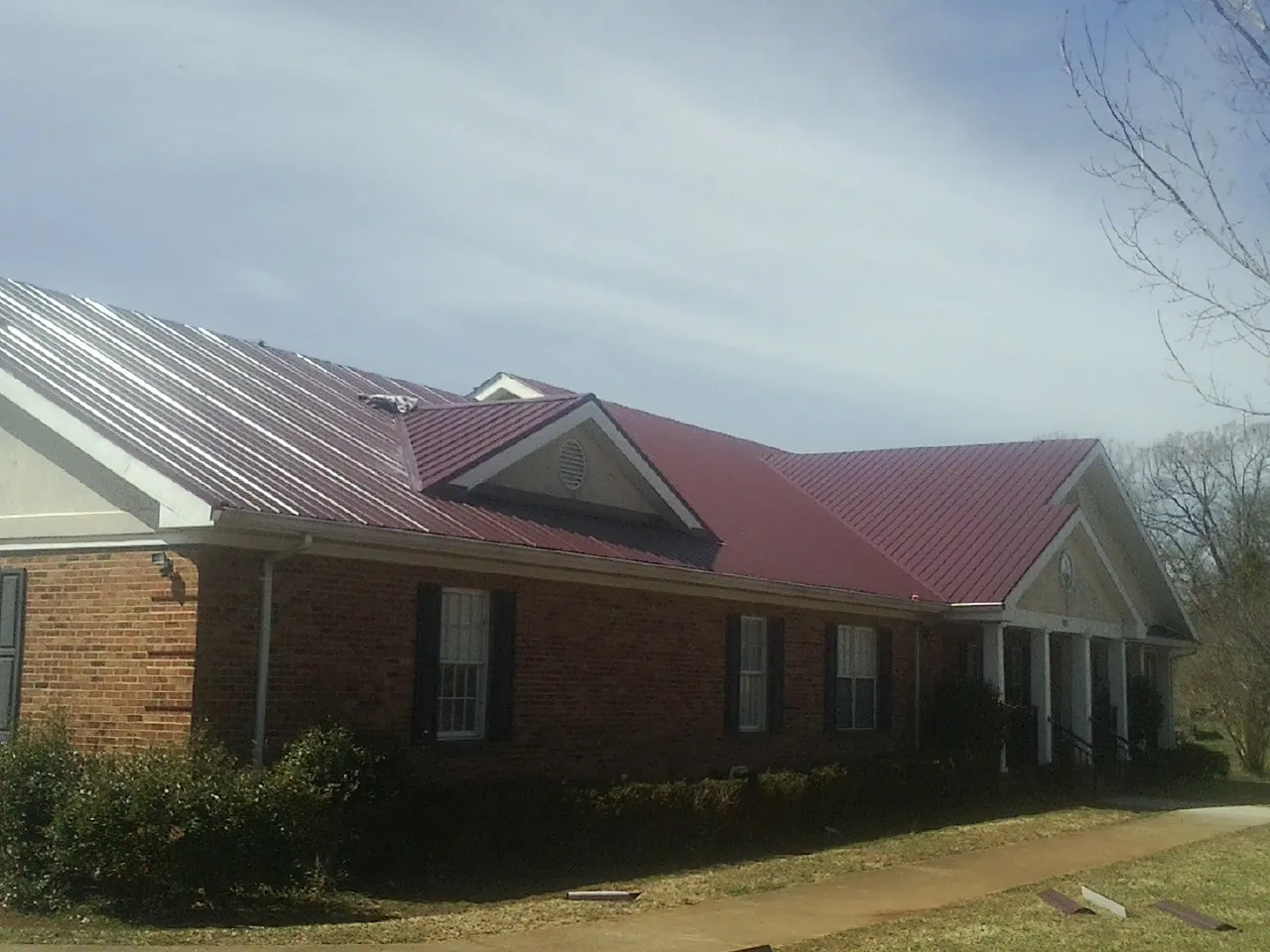 Red metal roof with gabled entries on a long brick building, from a Hail Damage Roof Repair job in Dandridge