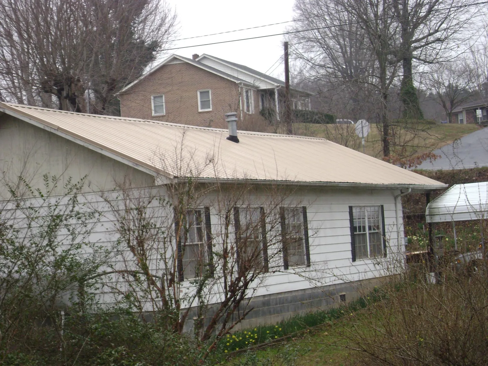 Tan metal roof on a white sided house set into a hillside — Commercial Roofing by Roofing Brothers in Dandridge